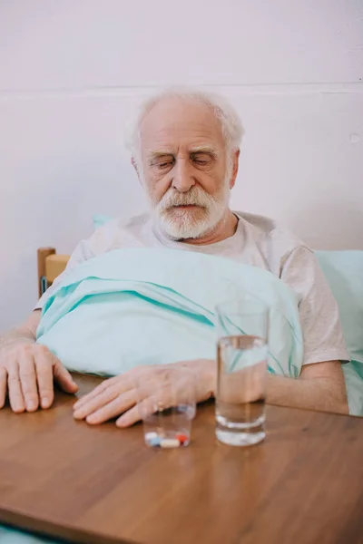 Old man looking sadly at pills on table — Stock Photo