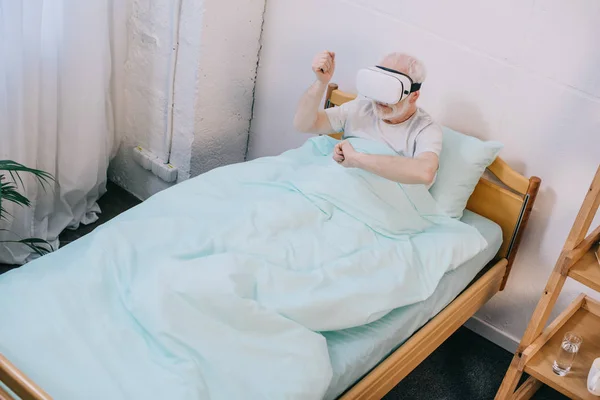 Paciente de edad avanzada en cama clínica usando auriculares vr - foto de stock