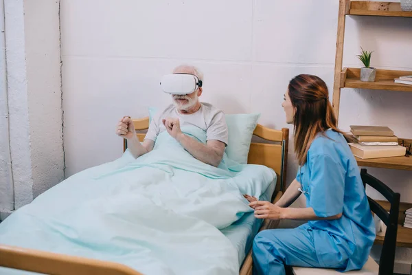 Nurse sitting by old man using vr glasses — Stock Photo