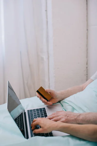 Крупним планом перегляд жінки, яка допомагає старшому пацієнту, використовуючи ноутбук та кредитну картку — стокове фото