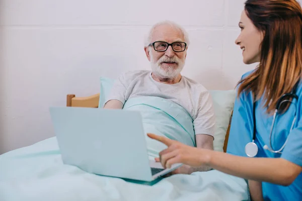 Медсестра сидит со старшим мужчиной с ноутбуком — стоковое фото