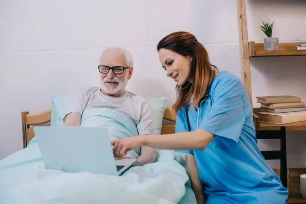 Enfermera señalando a la computadora portátil en manos de pacientes mayores - foto de stock