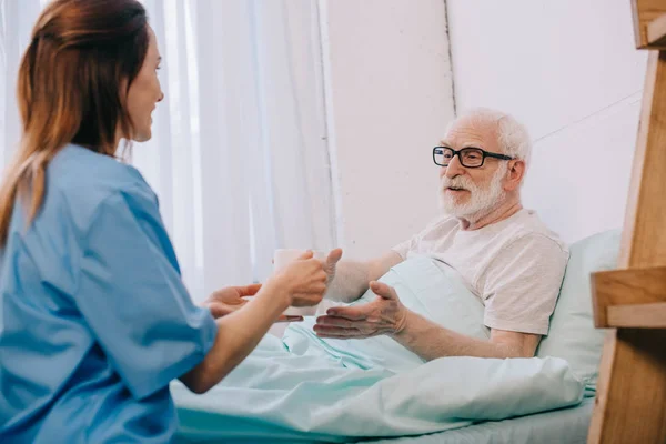 Nurse helping senior patient in bed to hold a cup — Stock Photo