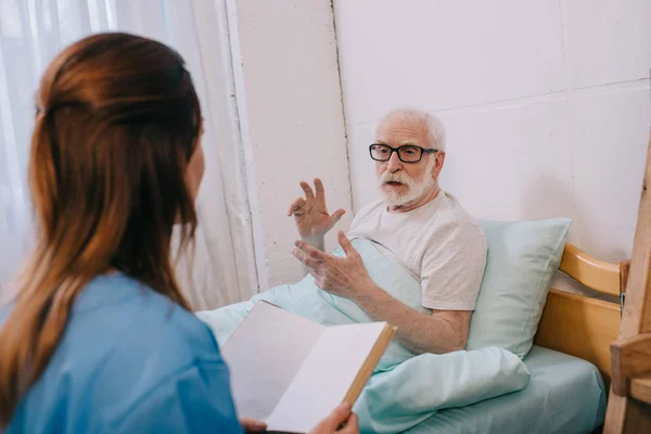 Vieil homme patient et infirmière discuter intrigue du livre — Photo de stock