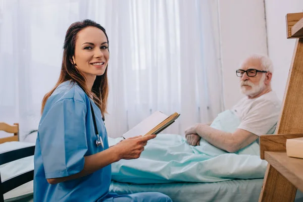 Krankenschwester und älterer Mann lesen Buch — Stockfoto