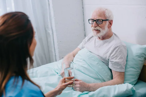 Krankenschwester gibt alten Mann im Bett ein Glas Wasser — Stockfoto