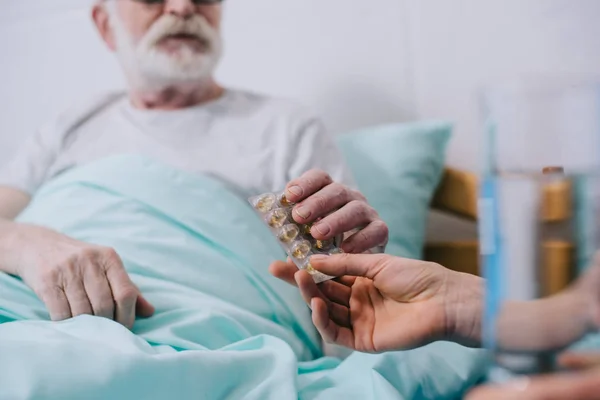 Vista de cerca del médico dando pastillas al paciente mayor en la cama - foto de stock