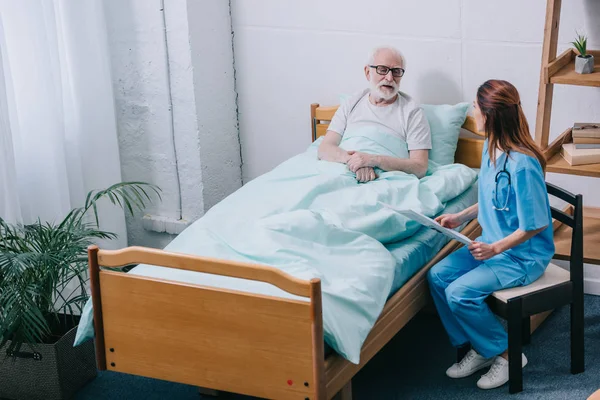 Paciente anciano y enfermera discutiendo noticias del periódico - foto de stock