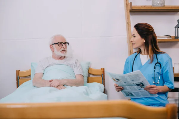 Enfermera leyendo periódico a paciente mayor - foto de stock