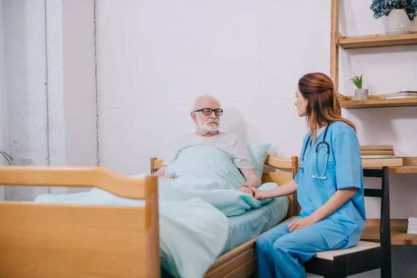 Infirmière par patient âgé masculin au lit — Photo de stock