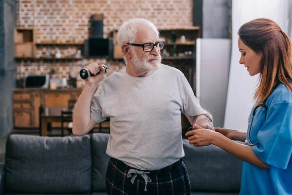 Медсестра помогает старшему мужчине тренироваться с гантелями — стоковое фото