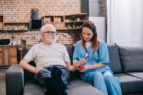 Female nurse checking heartbeat of senior man — Stock Photo