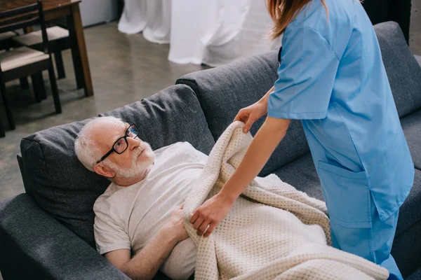 Enfermera ayudando a viejo paciente a cubrir con cuadros - foto de stock