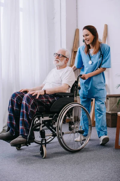 Enfermera empujando silla de ruedas con paciente senior - foto de stock