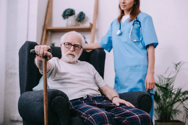 Enfermera de pie detrás de un hombre mayor con bastón - foto de stock