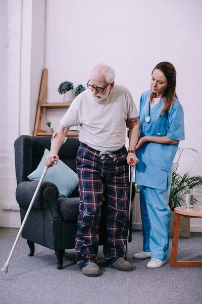 Infirmière soutenant le patient masculin avec des béquilles — Photo de stock