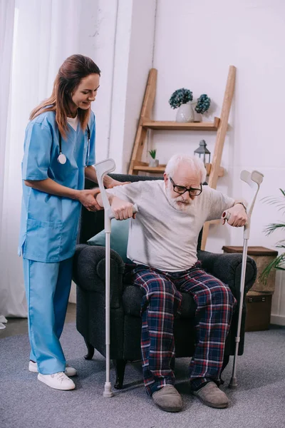 Enfermeira segurando paciente masculino com muletas — Fotografia de Stock