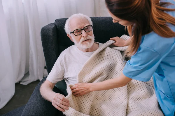 Aide soignant couvrant le patient âgé avec des carreaux — Photo de stock