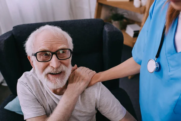 Nurse supporting and holding shoulder of smiling senior man patient — Stock Photo