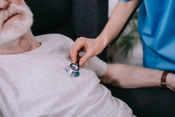 Крупный план женщины-медсестры со стетоскопом, проверяющей сердцебиение пожилого мужчины — стоковое фото