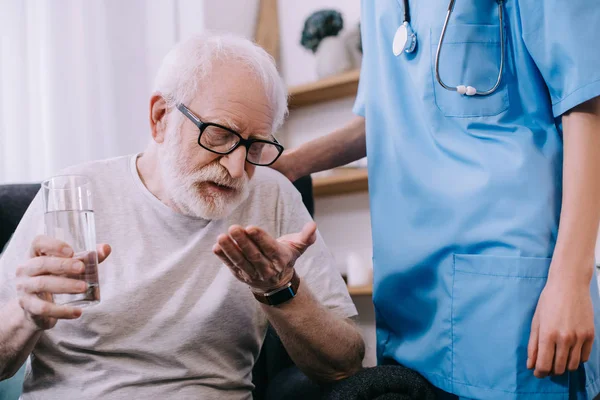 Смотритель рядом со старшим мужчиной, принимающим лекарства — стоковое фото