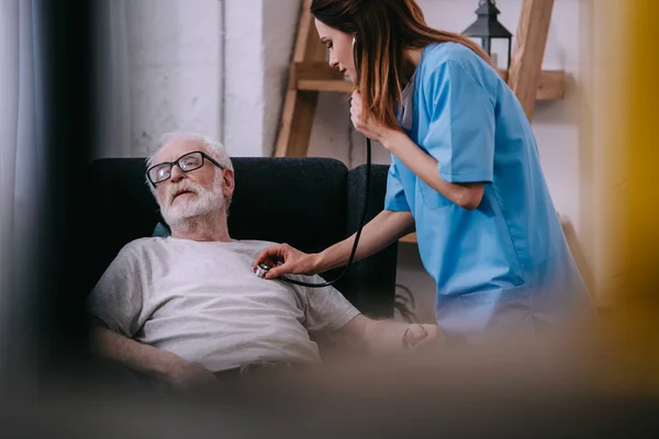 Медсестра со стетоскопом проверяет сердцебиение пожилого человека — стоковое фото