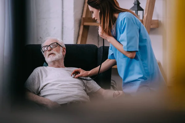 Infermiera con stetoscopio che controlla il battito cardiaco dell'uomo anziano — Foto stock