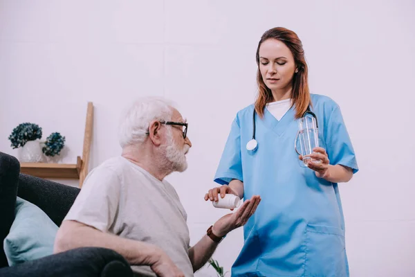 Nurse standing by senior man taking medications — Stock Photo