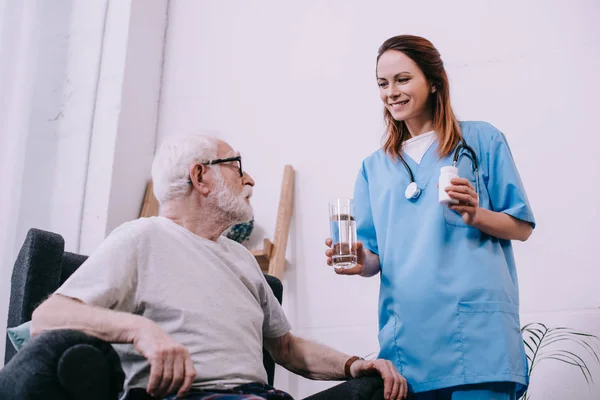 Медсестра, стоящая рядом со старшим мужчиной, принимающим лекарства — стоковое фото