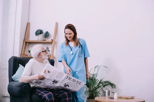 Enfermeira apontando jornal em mãos de paciente sênior — Fotografia de Stock