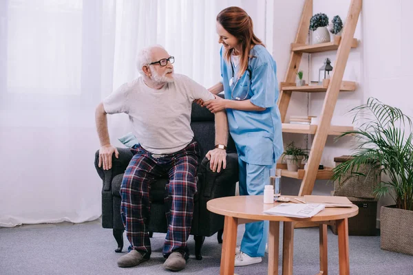 Enfermera ayudando a un hombre mayor a ponerse de pie - foto de stock