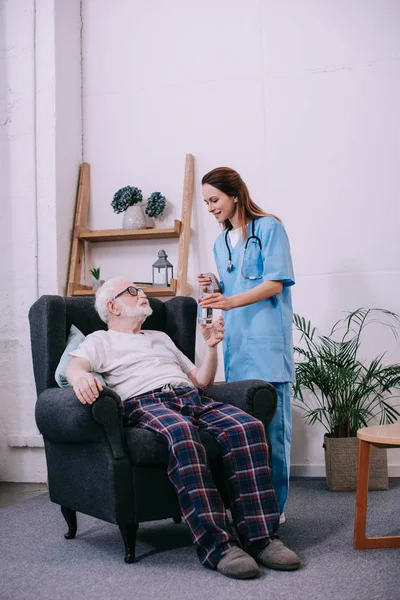Enfermera dando viejo hombre un vaso de agua - foto de stock