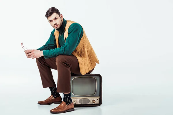 Bel homme de style rétro assis sur la télévision vintage et regardant la caméra sur blanc — Photo de stock