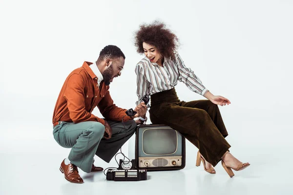 Afrikanisch-amerikanisches Paar im Retro-Stil schaut überrascht auf Vintage-Handy auf weiß — Stockfoto