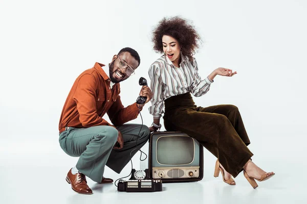 Feliz africano americano retro estilo pareja con vintage televisión y teléfono en blanco - foto de stock