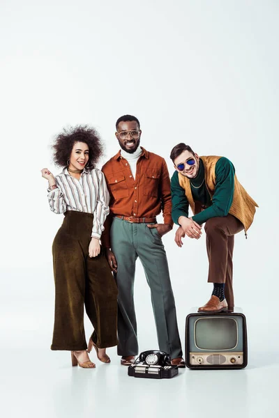 Sorridente multicultural retro estilo amigos com televisão vintage olhando para a câmera no branco — Fotografia de Stock