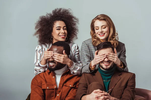 Happy multicultural retro styled girls covering eyes to multiethnic men isolated on grey — Stock Photo