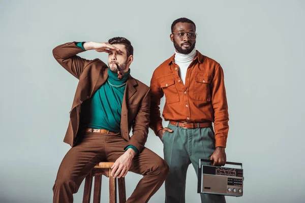 Multicultural retro styled friends with pipe and radio looking away isolated on grey — Stock Photo