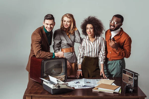 Smiling multicultural retro styled journalists looking at camera in office isolated on grey — Stock Photo