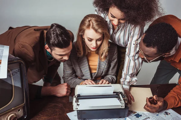 Multicultural retro styled journalists looking at text at typewriter — Stock Photo