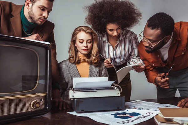 Amigos multiculturales de estilo retro que trabajan en la sala de redacción aislados en gris - foto de stock