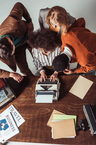 Vista aérea de periodistas multiculturales de estilo retro mirando cómo amigo escribir texto - foto de stock