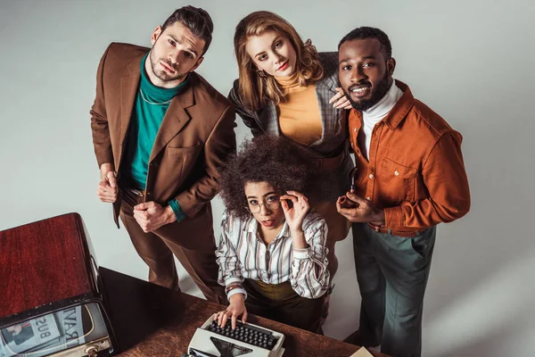 Vista aérea de amigos multiculturales de estilo retro con máquina de escribir mirando a la cámara - foto de stock