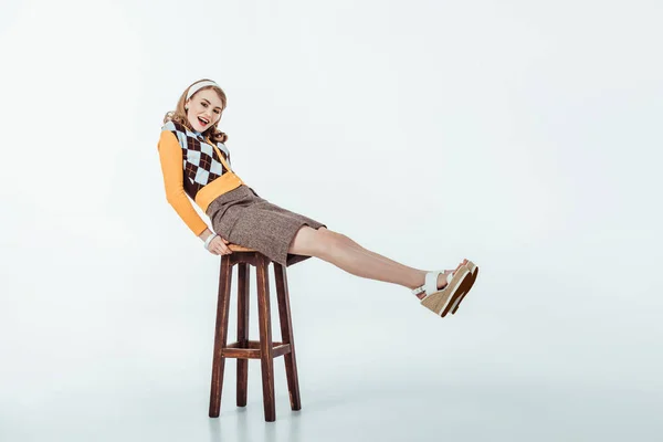 Smiling beautiful retro styled girl sitting on wooden chair and looking at camera on white — Stock Photo