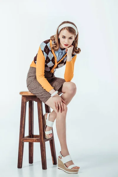 Beautiful retro styled girl sitting on wooden chair and looking at camera on white — Stock Photo