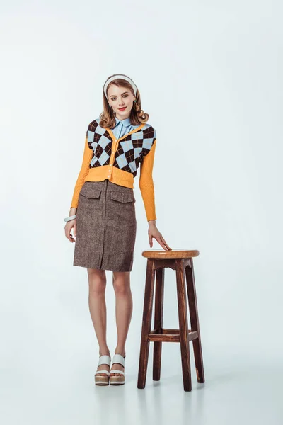 Beautiful retro styled girl standing near wooden chair on white — Stock Photo