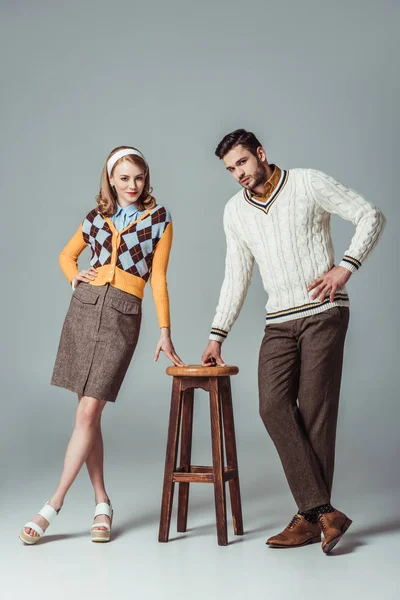 Beautiful retro styled couple posing with wooden chair on grey — Stock Photo