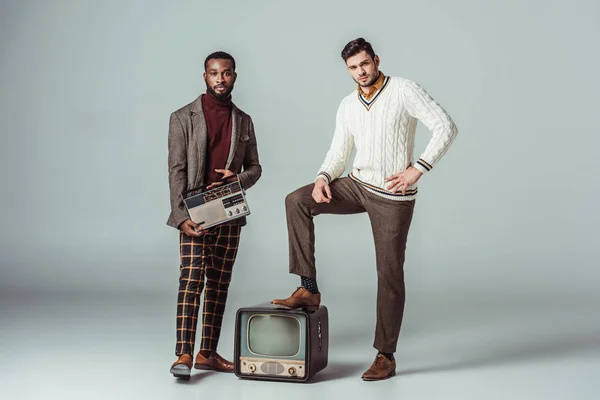 Multikulturelle Freunde im Retro-Stil posieren mit alten Radios und Fernsehern auf grau — Stockfoto