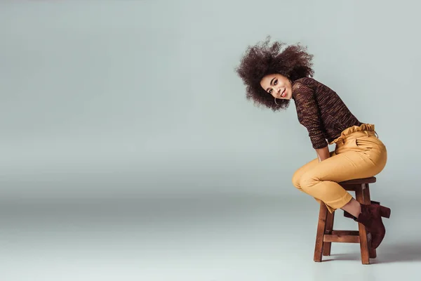 Mulher americana africana atraente em roupas retro sentado na cadeira em cinza — Fotografia de Stock