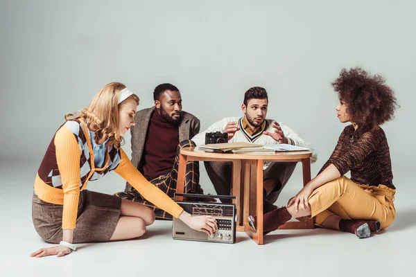 Multicultural retro styled friends sitting at table, girl tuning vintage radio — Stock Photo